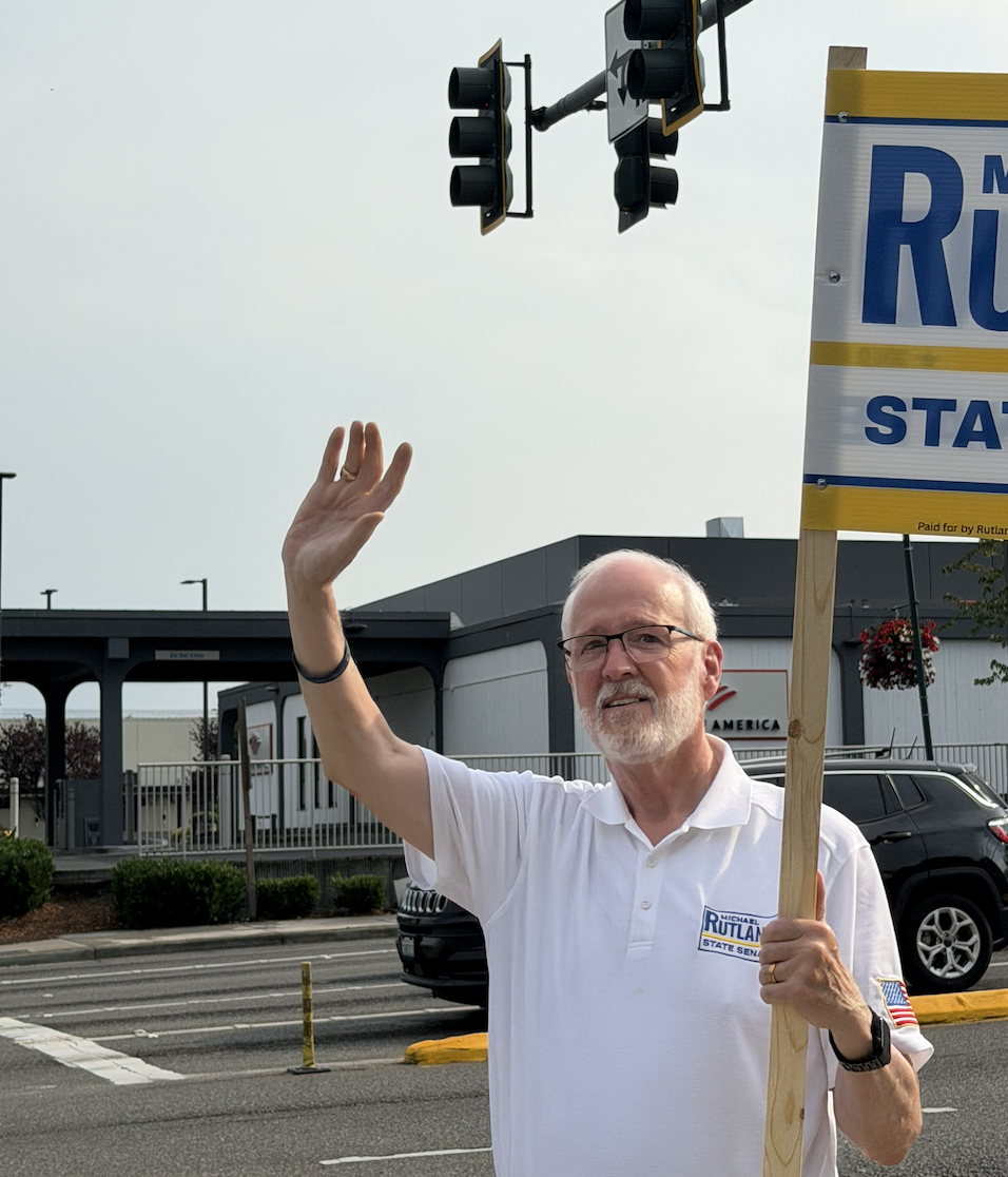 Michael Rutland waving to drivers while holding a campaign sign